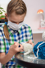 Image showing A girl in a medical mask is engaged in embroidery at home.