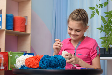 Image showing Girl knits a soft toy sitting at a table in the interior of a children\'s room