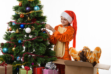 Image showing One girl hangs a ball on the Christmas tree, the other climbed into the box with her head