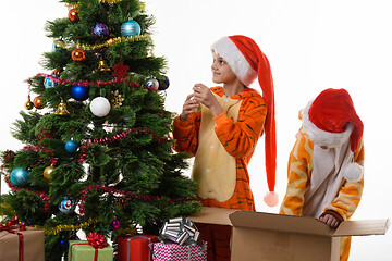 Image showing Girls decorate a Christmas tree, one of them delves into a box with toys