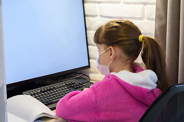 Image showing A girl in a medical mask sits at a computer and does homework, free space on the screen