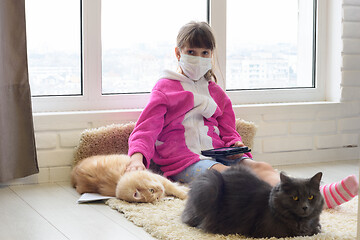 Image showing A sick quarantined girl sits on the floor with a tablet, cats are lying next to the carpet