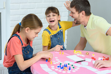 Image showing The girl and dad are screaming and laughing cheerfully, the other girl is considering the next move in the board game