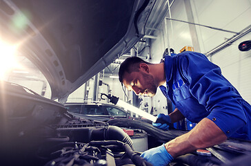 Image showing mechanic man with lamp repairing car at workshop