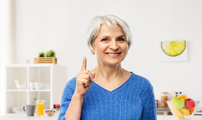 Image showing smiling senior woman pointing finger up in kitchen