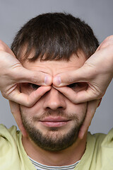 Image showing Close-up portrait of a man who made with his hands a kind of glasses on the eyes of European appearance