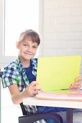 Image showing A girl with a tablet sits at a table at home and joyfully looked into the frame