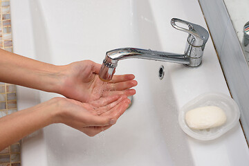 Image showing Girl pours water in the palm of the hand in the bathroom