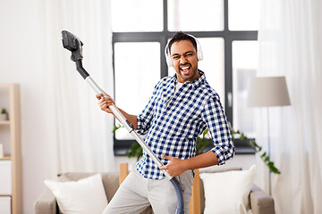 Image showing man in headphones with vacuum cleaner at home