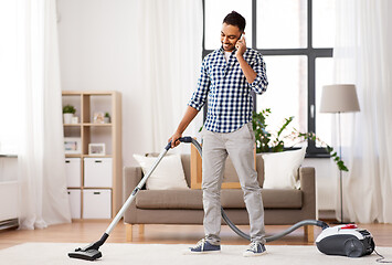 Image showing man with vacuum cleaner calling on cell at home