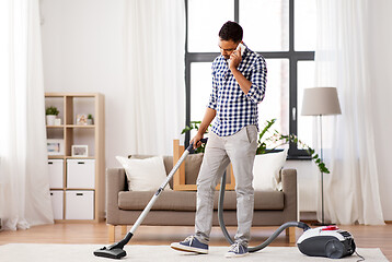 Image showing man with vacuum cleaner calling on cell at home