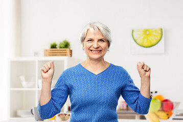 Image showing happy senior woman celebrating success in kitchen