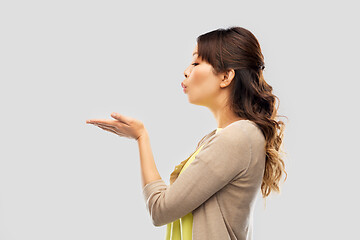 Image showing asian woman holding something on hand and blowing