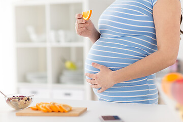 Image showing close up of pregnant woman eating orange at home