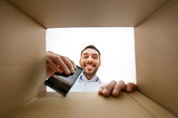 Image showing smiling man taking smartphone out parcel box