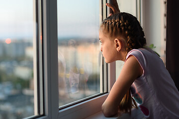 Image showing Girl bored at home in quarantine looks out the window