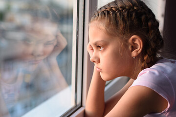 Image showing Tired of self-isolation, a bored quarantine girl looks out the window