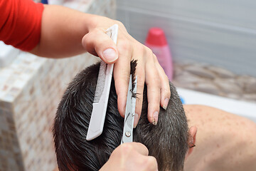 Image showing The hairdresser cuts the hair on the head of a man, working at home from a client in the bathroom