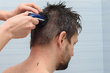 Image showing Girl cuts hair with a clipper on a man\'s head at home in the bathroom