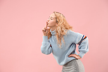 Image showing The young woman whispering a secret behind her hand over pink background