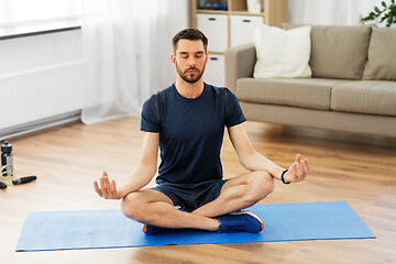 Image showing man meditating in lotus pose on yoga mat at home