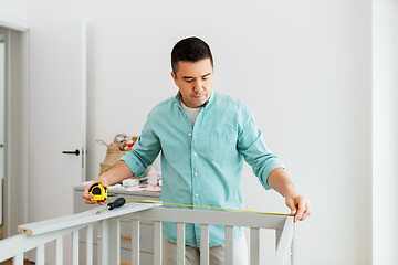 Image showing father with tablet pc and ruler measuring baby bed