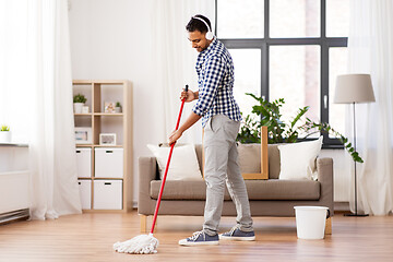 Image showing man in headphones with mop cleaning floor at home