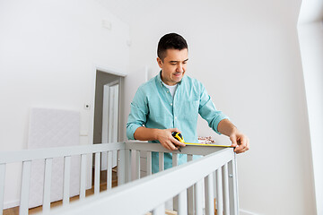 Image showing father with tablet pc and ruler measuring baby bed