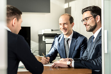 Image showing Group of confident successful business people reviewing and signing a contract to seal the deal at business meeting in modern corporate office.