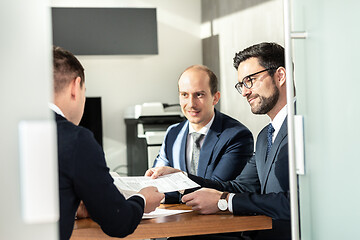 Image showing Group of confident successful business people reviewing and signing a contract to seal the deal at business meeting in modern corporate office.