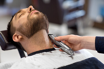 Image showing man and barber with trimmer cutting beard at salon