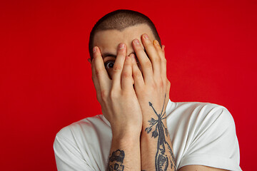 Image showing Caucasian young man\'s portrait on red studio background, emotinal and expressive