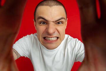 Image showing Caucasian young man\'s portrait on red studio background, emotinal and expressive