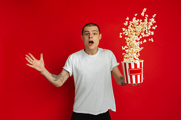 Image showing Caucasian young man\'s portrait on red studio background, emotinal and expressive, cinema concept