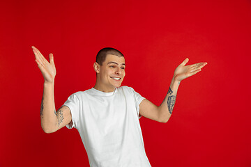 Image showing Caucasian young man\'s portrait on red studio background, emotinal and expressive