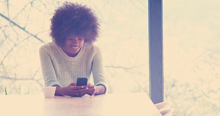 Image showing black woman drinking coffee and using a mobile phone  at home