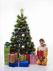 Image showing A child holds a gift while sitting by the Christmas tree