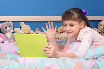 Image showing A schoolgirl studies remotely at home, lies in bed and watches a video lesson