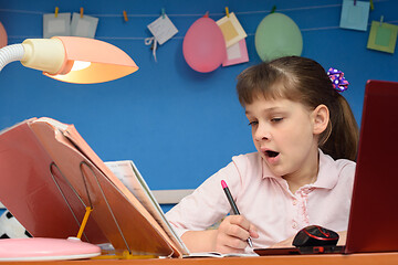 Image showing The girl does lessons for a long time and yawns while sitting at the table