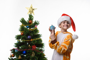 Image showing The girl at the Christmas tree shows a Christmas toy