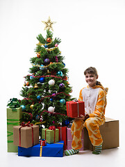 Image showing Happy little girl sits by the Christmas tree and holds a New Year\'s gift