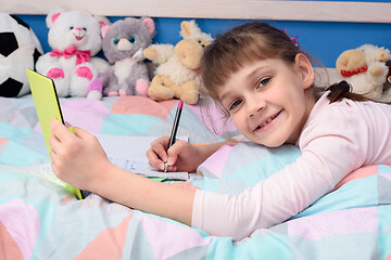 Image showing A schoolgirl studies remotely at home, lies in bed and watches a video lesson