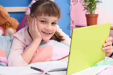 Image showing Happy girl lying at home in bed and watching school video lessons