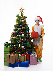 Image showing A girl stands with a red gift near the Christmas tree