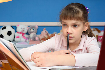 Image showing The girl does homework at home and, thinking, stuck a pen in her nose