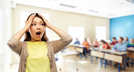 Image showing stressed asian woman holding to her head at school