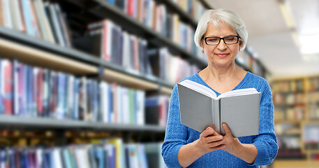 Image showing senior woman in glasses reading book at library