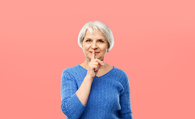 Image showing senior woman making shush gesture over pink