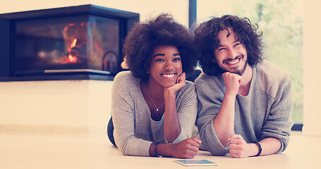 Image showing multiethnic couple lying on the floor  in front of fireplace