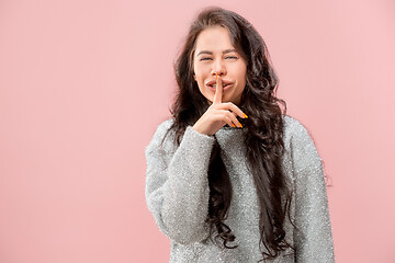 Image showing The young woman whispering a secret behind her hand pink background